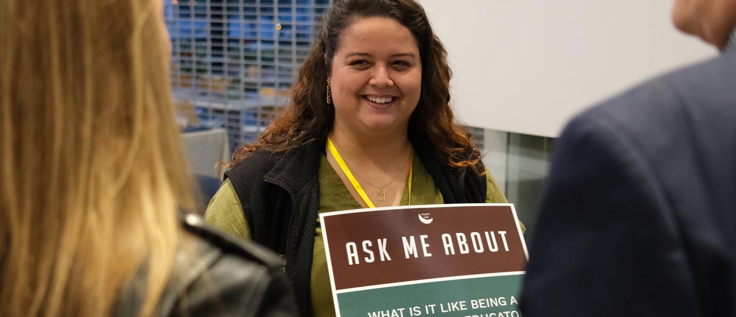 Educator holding an "Ask Me About" sign
